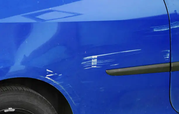 Scratches and dents on a blue car. Accidental damage to a car