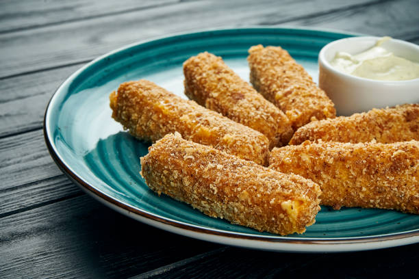 istock Delicious close up view on Deep-fried fish or cheese sticks fried with white sauce on a blue plate on a black background. Bar snack for beer. 1197898036