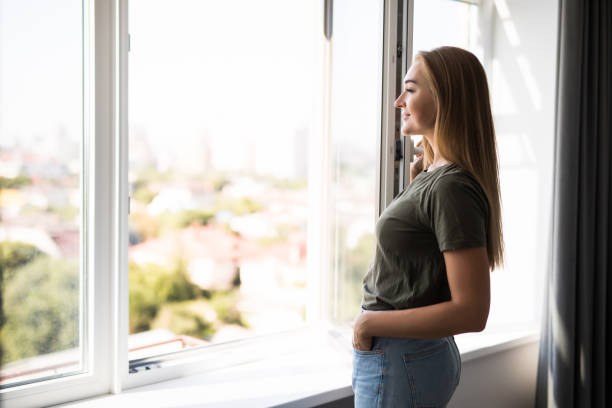 mujer joven abriendo ventana en la sala de estar en casa - window sun sunlight vertical fotografías e imágenes de stock