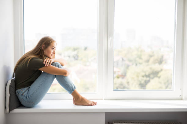 istock Sad depressed young woman having social problems sitting on windowsill 1197903049