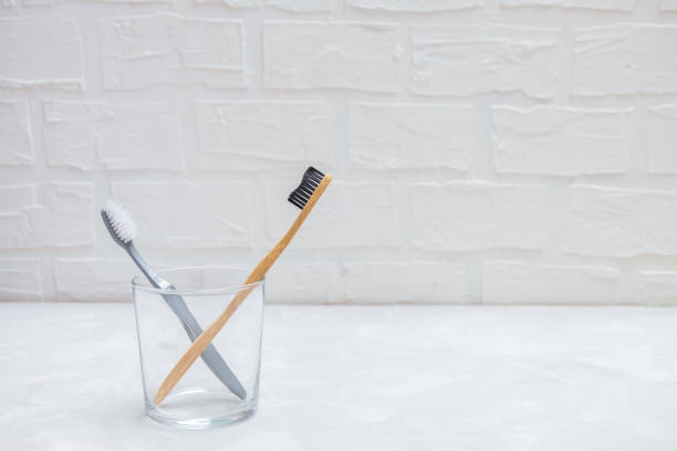 istock Plastic toothbrush and eco-friendly bamboo toothbrush in a glass cup on grey neutral background 1197904346