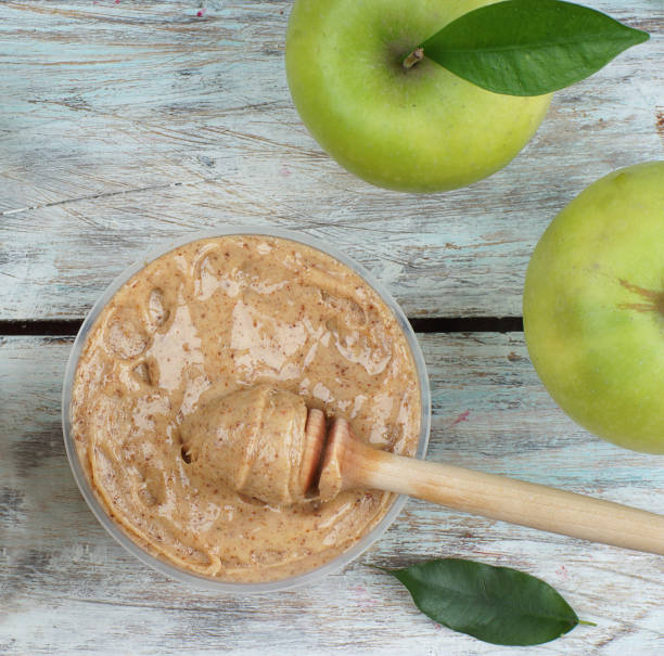 istock Beaten honey in a jar and a green apple on a light table, top view 1197906053