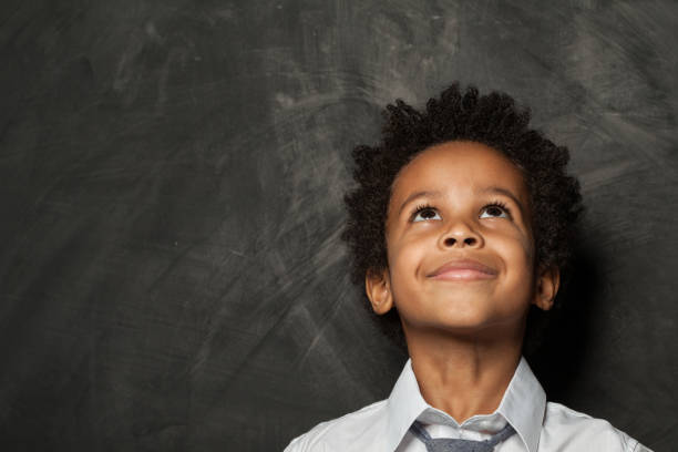 istock Little child boy looking up on blackboard background 1197913297