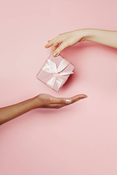 Present box in female hand on pink background. Abstract gift concept