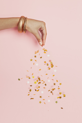 Beautiful female hand streams sparkling gold stars confetti on pink background