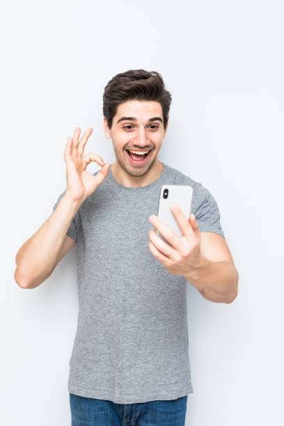 istock Happy young man waving to a smart phone camera isolated on white background 1197919712