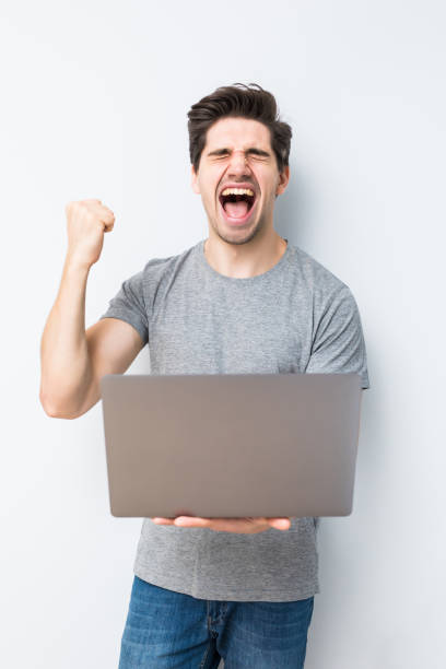 istock Emotional young man with laptop celebrating victory on white background 1197920871
