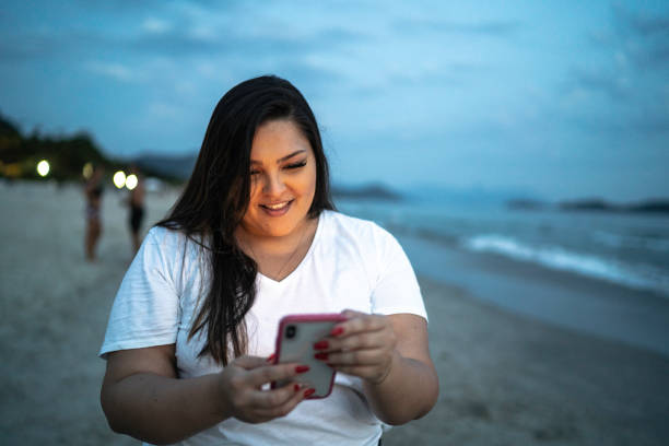 istock Young happy woman on the beach walking and using smart phone at night 1197925037