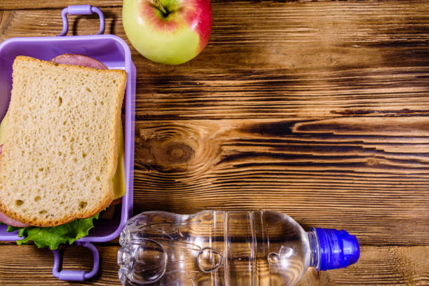 спелое яблоко, бутылка воды и коробка для обеда с бутербродами на деревянном столе. вид сверху - lunch box packed lunch school lunch lunch стоковые фото и изображения