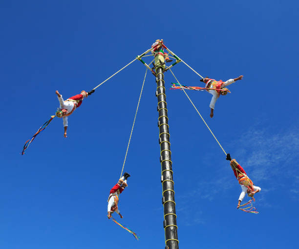 The Voladores, or flyers performance. They climb up a very high pole their waist to ropes wound around the pole and then jump off, flying gracefully around it. Riviera Maya, Mexico- December 27, 2019: The Voladores, or flyers performance. They climb up a very high pole their waist to ropes wound around the pole and then jump off, flying gracefully around it. volador stock pictures, royalty-free photos & images