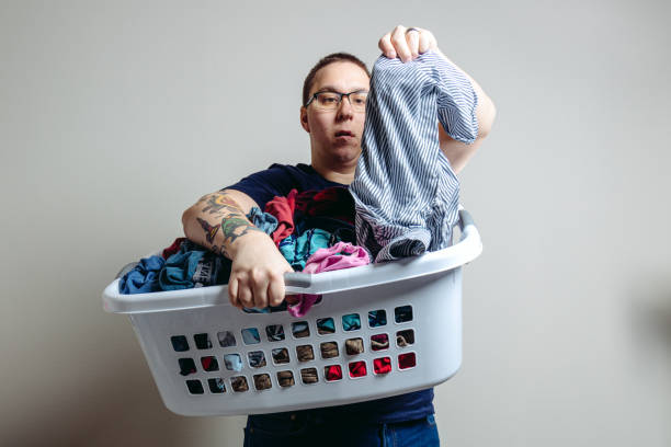 Father with Tattoos Does Laundry Studio stock photos of a Husband and Father with Tattoos doing laundry. He is wearing a navy blue shirt dressed casually for household chores like laundry. laundry husband housework men stock pictures, royalty-free photos & images