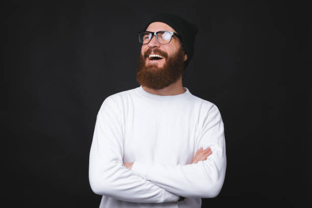 istock A young bearded man is smiling and standing with crossed hands on black background. 1197937355