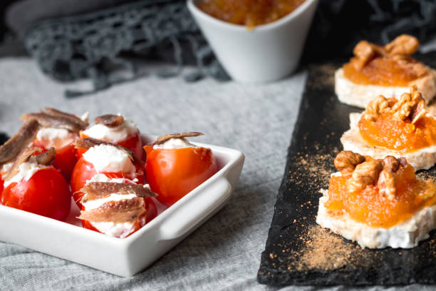 still life of goat roll cheese with jam and walnuts with cherry tomatoes stuffed with cheese and anchovies. top view - food dinner prepared fish gourmet imagens e fotografias de stock