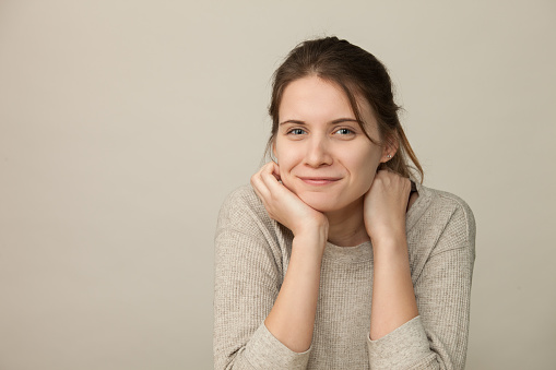 Close-up studio portrait of an attractive 20 year old woman with long brown hair in a beige sweater on a beige background