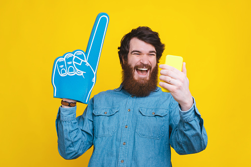 Cheerful young man in blue shirt looking at smartphone and celebrating