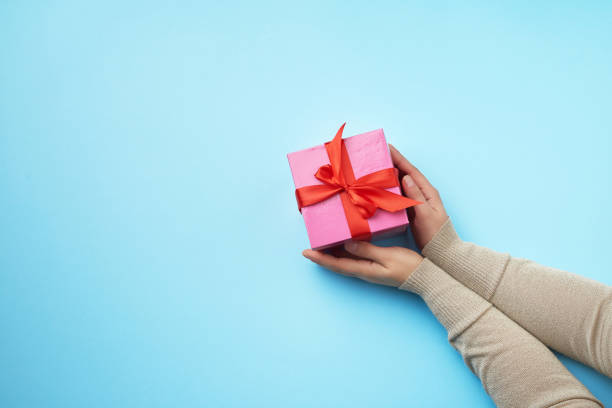 istock two female hands in a sweater hold closed square pink box with a bow on a blue background 1197946278