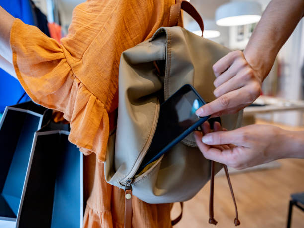 Close up shot of female thief trying to steal a smartphone while customer is looking at clothes in a store Close up shot of female thief trying to steal a smartphone while customer is looking at clothes in a store - Criminal lifestyles pickpocketing stock pictures, royalty-free photos & images