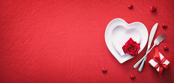 Red table setting cutlery with hearts decoration, gift box and rose for valentines days dinner