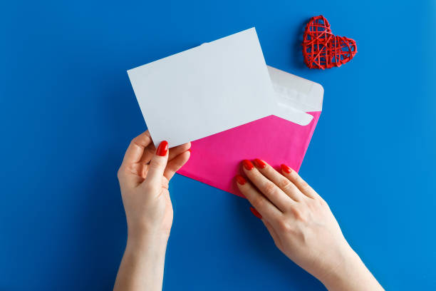 istock Pink envelope with a blank card in hands on a blue background. 1197975596