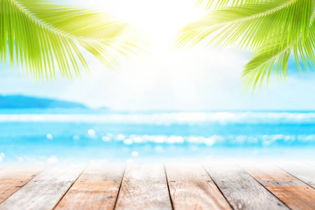 istock Blur tropical beach with bokeh sun light wave and palm tree on copy space empty old wood table abstract background. 1197979887