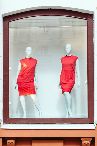 Two mannequins of a female figure in red dresses in a shop window.