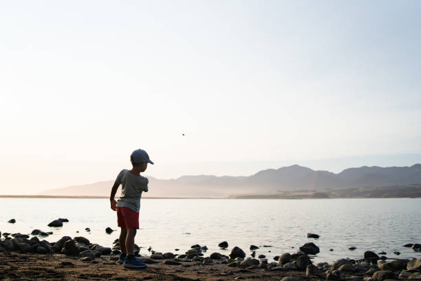 Boy throwing stone into the sea at summer day