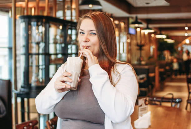 Young charming woman plus size drinking milkshake in hand in cafe, enjoing life and her appearance Young charming woman plus size with milkshake in hand in cafe, enjoing life and her appearance plus size woman fashion laughing stock pictures, royalty-free photos & images
