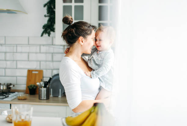 young woman mom with baby girl on hands havinh fun and cooking breakfast on bright kitchen at home - breakfast family child healthy eating imagens e fotografias de stock