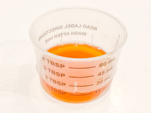 measuring cup of liquid cough or cold syrup medicine - cough medicine spoon medicine tablespoon imagens e fotografias de stock