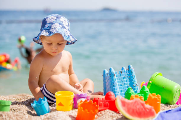 Beautiful two years old toddler child, boy, playing with beach toys on the beach coast near water Beautiful two years old toddler child, boy, playing with beach toys on the beach coast near water, summer time sun hat stock pictures, royalty-free photos & images