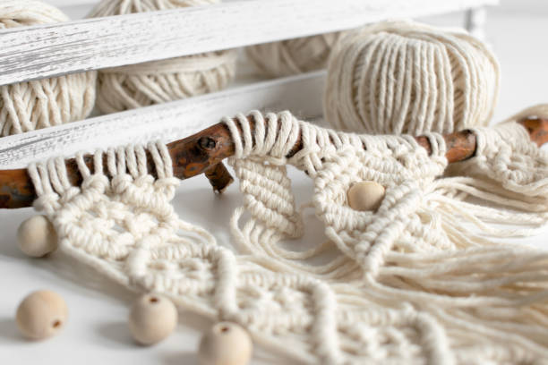 Handmade macrame braiding and cotton threads on rustic wooden stick. Boho image good for macrame and rustic handicrafts banners and advertisement stock photo