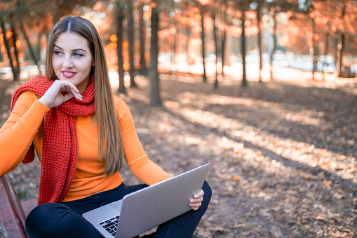 Smiling beautiful girl using laptop computer in the park environment a