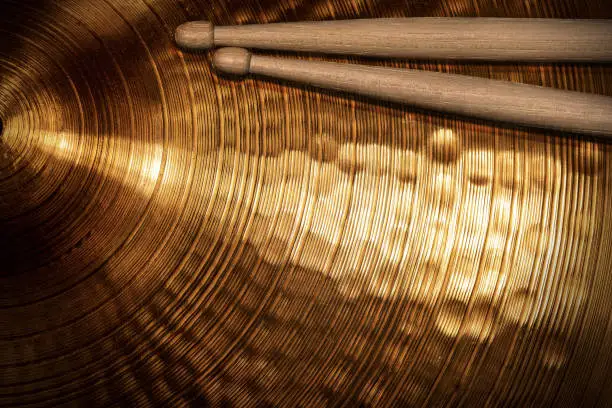 Close-up of two wooden drumsticks on a golden colored cymbal. Percussion instrument