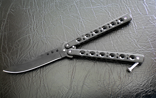 Butterfly knife black against black leather close-up. Bandit weapons.