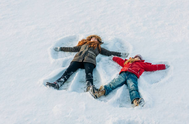 tutta la lunghezza delle ragazze che fanno angeli della neve - two girls only cheerful front view horizontal foto e immagini stock