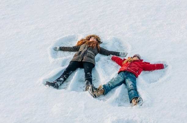Full length of girls making snow angels High angle view of sisters making snow angels. Full length of girls are lying on snow. They are enjoying during winter. children in winter stock pictures, royalty-free photos & images