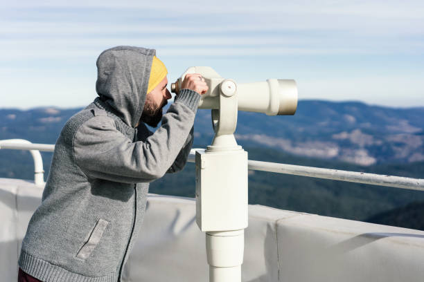 Side-view image of young male hiker looking through tourist binoculars