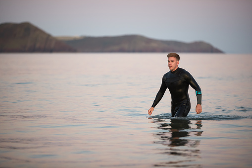 Hombre usando traje de neopreno vadeando a través del mar poco profundo por la costa photo
