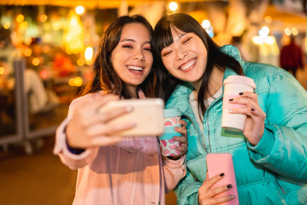 ソーシャルネットワークアプリ用のスマートフォンでビデオを作る幸せなアジアの友人 - 新しい技術トレンドを楽しむ若い女性 - 友情、技術とインフルエンサーのコンセプト - 顔に焦点を当� - 女性 写真 ストックフォトと画像