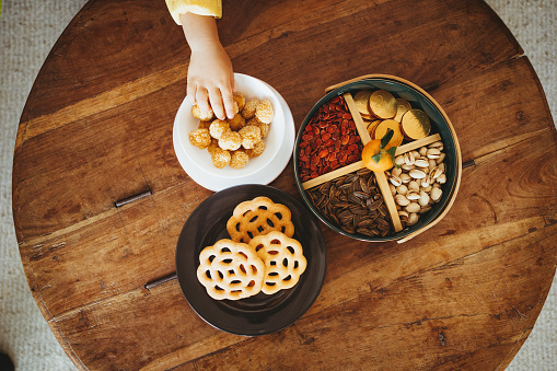Overhead view of kid's hand grabbing traditional Chinese snacks for Chinese New Year from the wooden table
