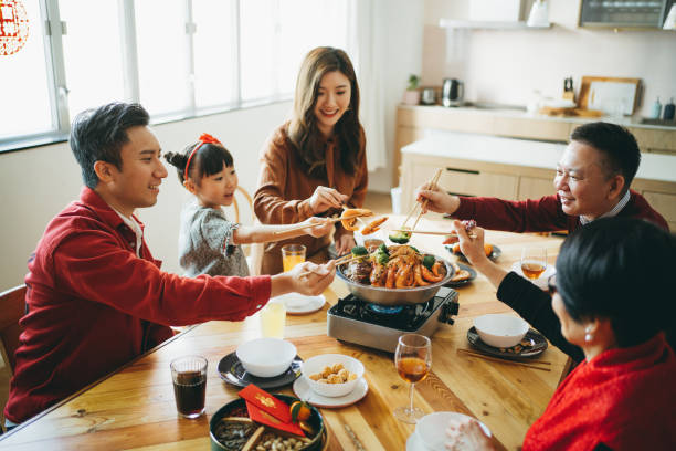 Three generations of joyful Asian family celebrating Chinese New Year and enjoying scrumptious traditional Chinese poon choi on reunion dinner Three generations of joyful Asian family celebrating Chinese New Year and enjoying scrumptious traditional Chinese poon choi on reunion dinner china chinese ethnicity smiling grandparent stock pictures, royalty-free photos & images