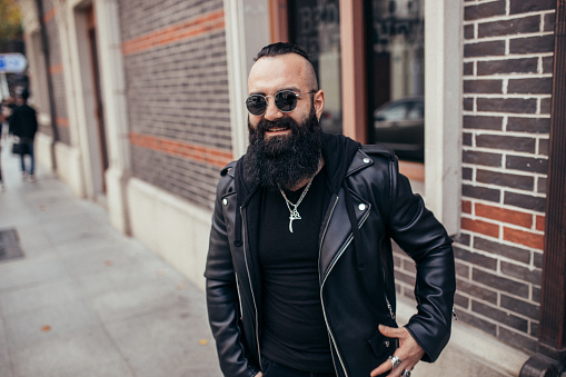 Handsome bearded man in leather jacket is standing outside.