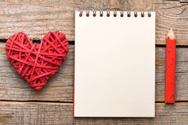 Empty notebook, pen and heart on a wooden table. Top view, concept on Valentine`s day. Empty space in the notebook to enter text or graphics.