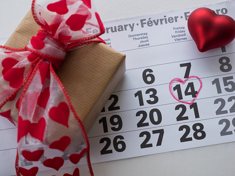 Calendar page with highlighted heart written in red on February 14 of Valentine's Day with red heart combination, gift box. Top view with space for greetings. Concept of Valentine's day, holiday