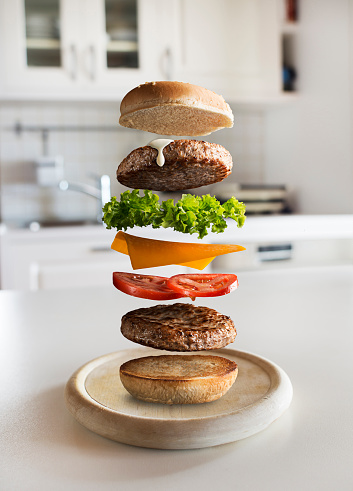 Maxi hamburger with flying ingredients placed in the kitchen. Conceptual jumping Burger. Delicious and attractive hamburger with refreshing ingredients