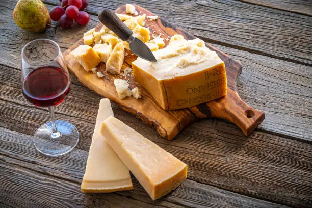 Parmesan Reggiano cheese on cutting board knife with wine and fruits on table