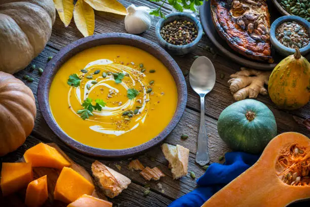 Autumn pumpkin soup and ingredients on rustic wooden table