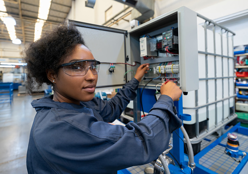 Black woman working at a manufacturing watre pump plant smiling at camera wearing protective goggles