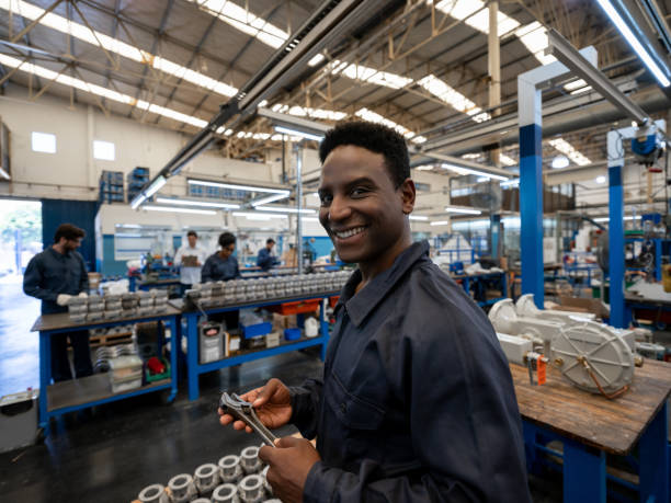istock Friendly african american blue collar worker holding an adjustable wrench smiling a camera at a manufacturing plant 1198042345