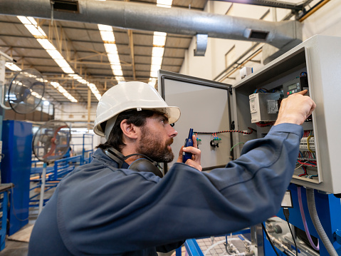 Latin american engineer checking a switch board and using a walkie- talkie at a manufacturing plant - Industrial concepts